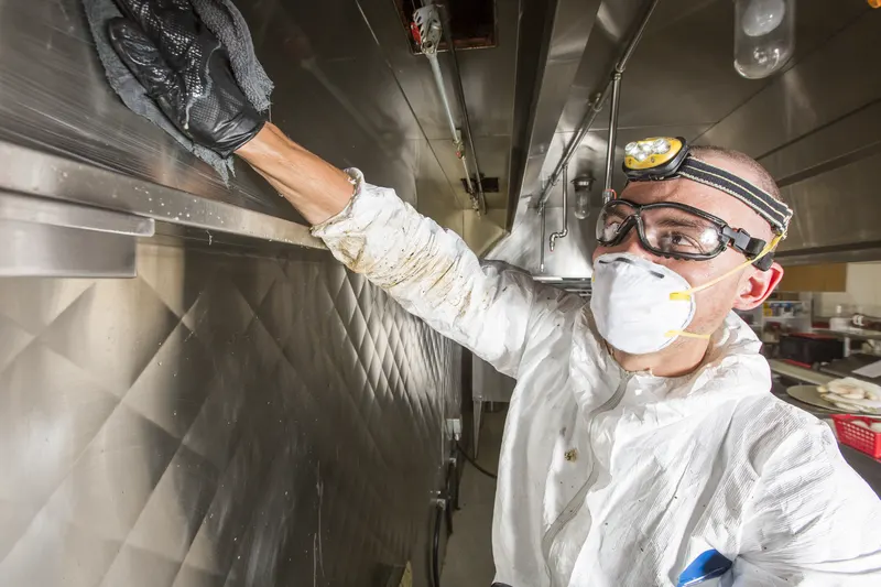 Technician reaching into the plenum chamber behind a removed baffle filter of a commercial kitchen exhaust hood