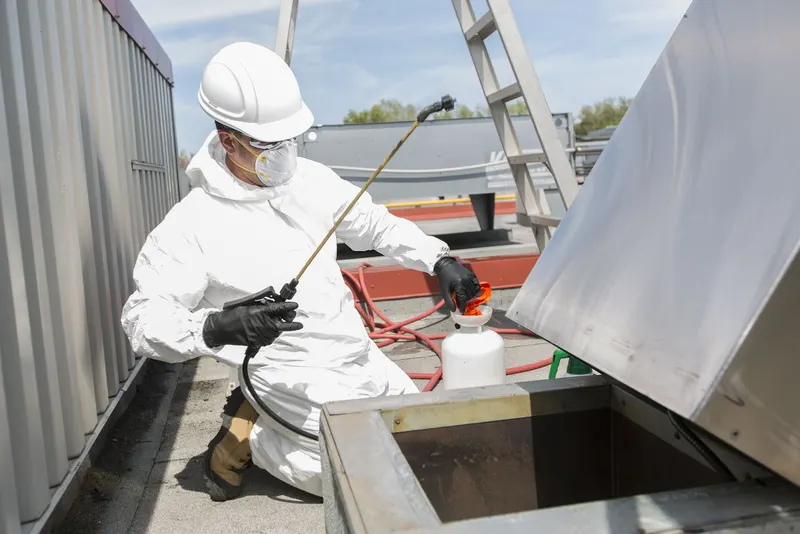 Rooftop kitchen exhaust fan tipped back on its hinge while a technician cleans the inside of the housing