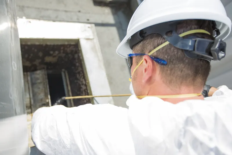 Technician in a hard hat working at an opened access hatch on a commercial kitchen exhaust duct