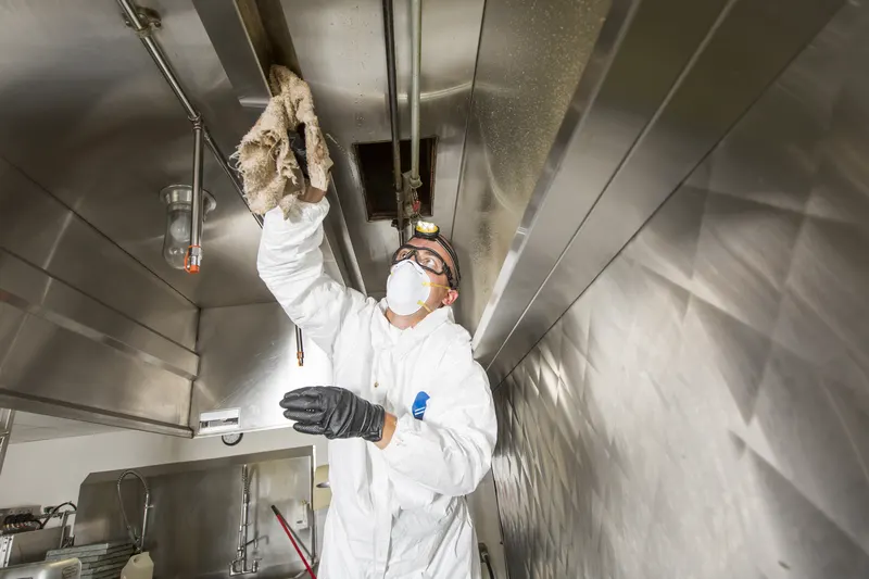 Technician wiping the plenum ceiling above the filter bank inside a commercial kitchen exhaust hood