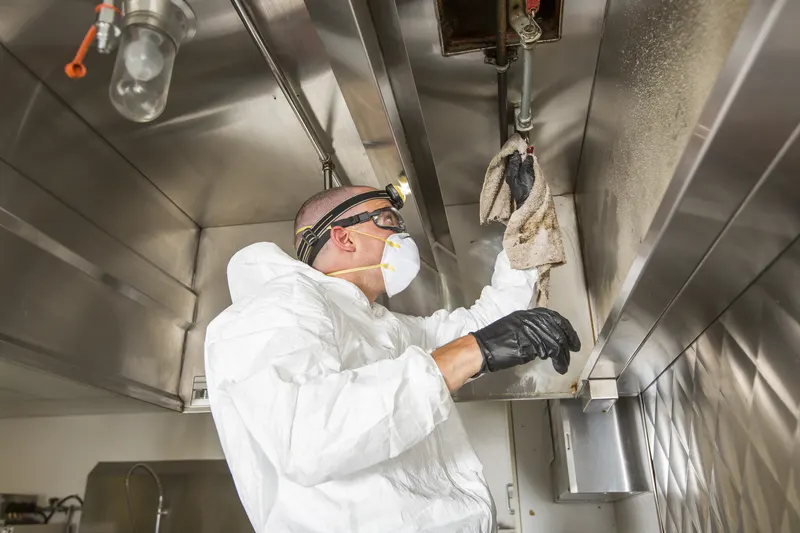 Technician wiping the lower edge of a stainless exhaust canopy beside the hood light