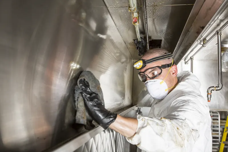 Technician hand wiping grease from the interior wall of an exhaust duct